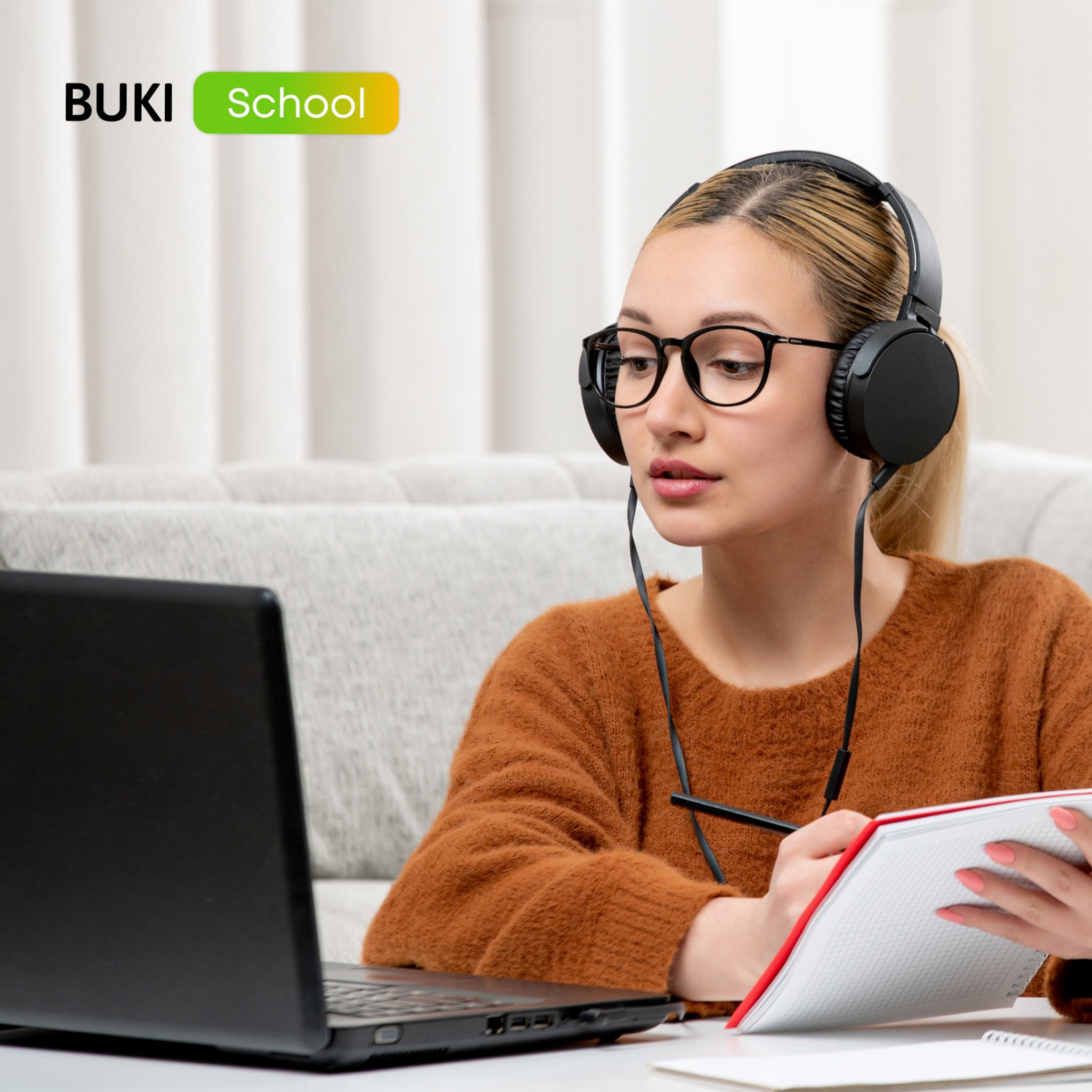 Kobieta w słuchawkach, z laptopem i notatnikiem, uczestniczy w lekcji online BUKI School. Ciepłe światło, stonowane tło, skupienie na twarzy.