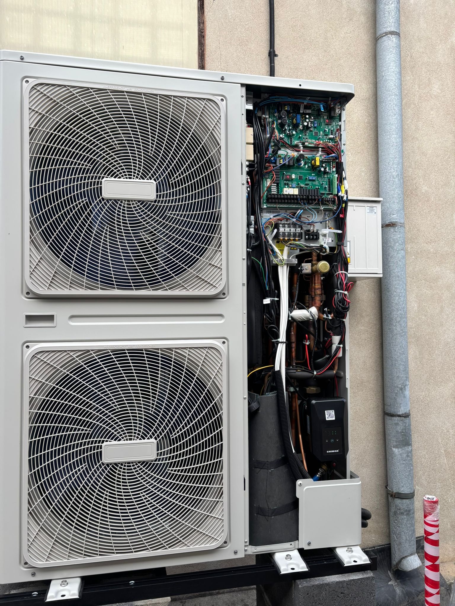 Otwarta obudowa klimatyzatora z widocznymi elementami wewnętrznymi, w tym przewodami i płytkami drukowanymi. Dwa wentylatory z przodu. Rura spustowa obok.