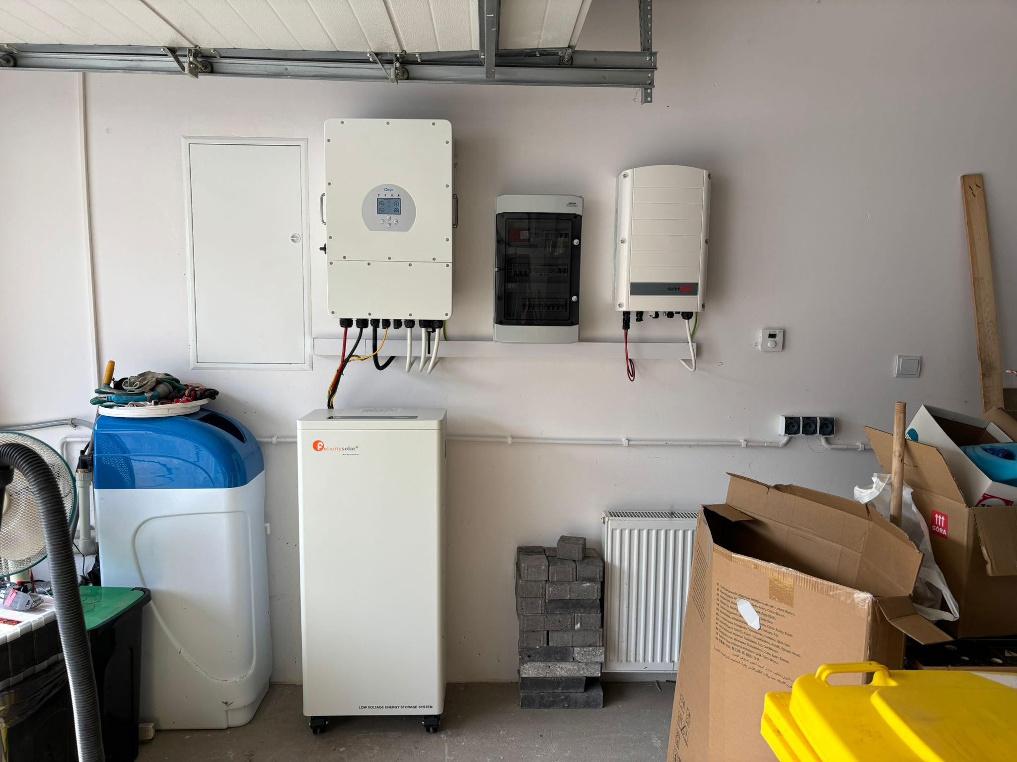 Kompletna instalacja fotowoltaiczna w garażu: inwerter, rozdzielnica, magazyn energii Felicitysolar, falownik SolarEdge. Widoczne okablowanie i elementy montażowe.