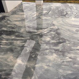 DS-eco Sp zoo - Szara, błyszcząca posadzka żywiczna na tarasie zewnętrznym, z unikalnym wzorem przypominającym marmur, widoczna z góry, z fragmentem okna i słupa w tle.