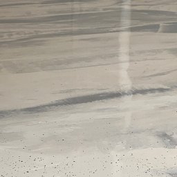 DS-eco Sp zoo - Jasnoszara, błyszcząca posadzka z delikatnym wzorem przypominającym marmur i drobnymi, ciemnymi inkluzjami. Widoczne refleksy światła podkreślają gładką powierzchnię.