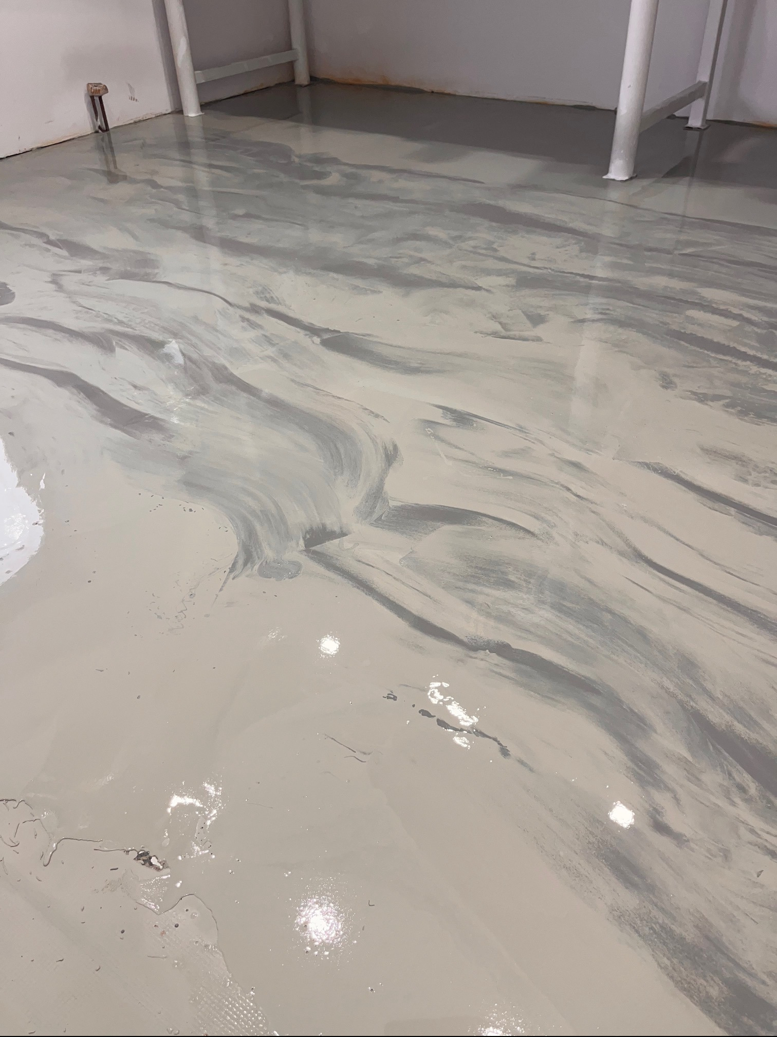 Błyszcząca, jasnoszara posadzka z efektem marmuru w garażu, z widocznymi białymi rurami przy ścianie. Gładka powierzchnia odbija światło.