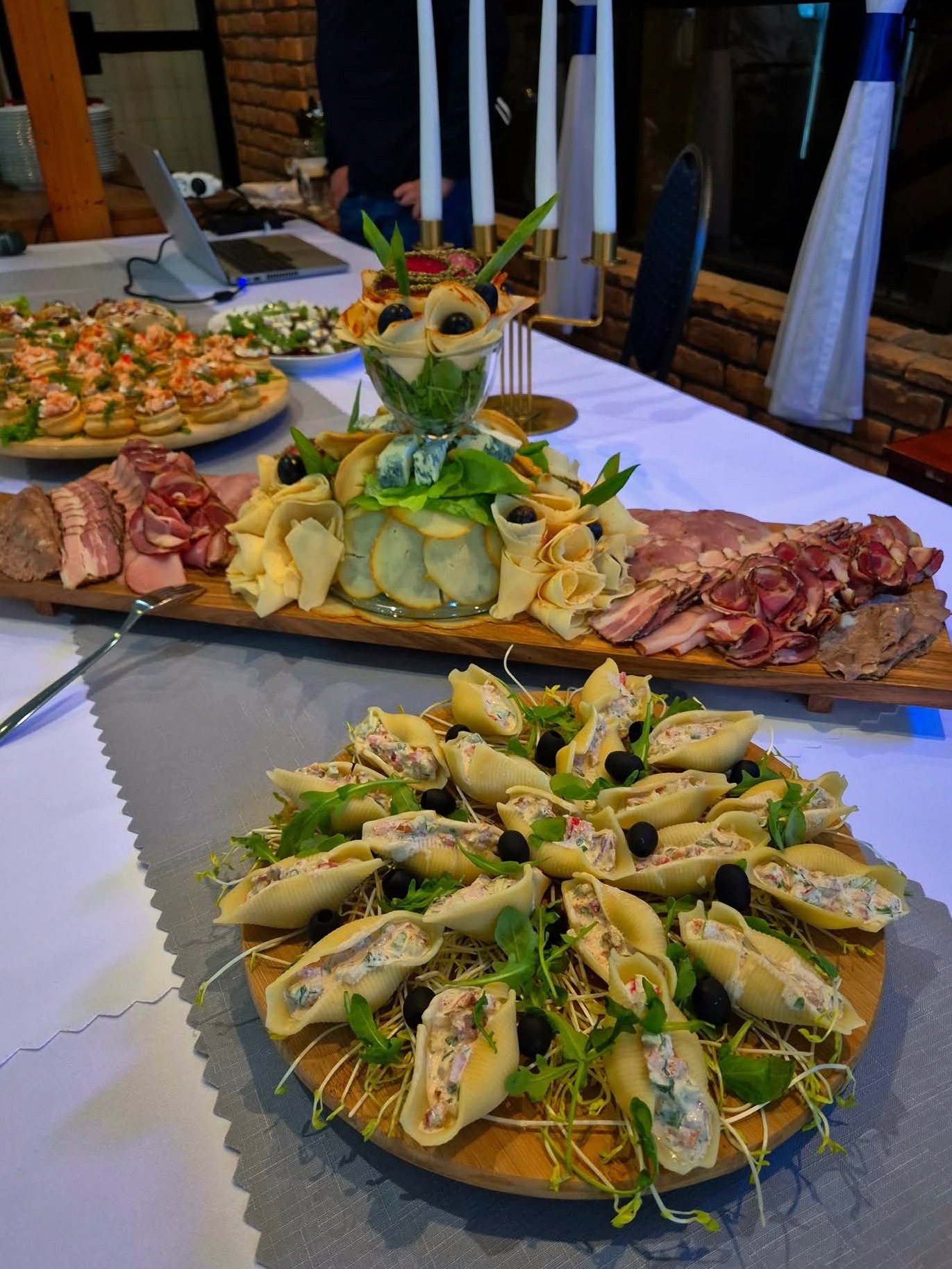 Dekoracyjny stół z przekąskami: muszle makaronowe z farszem, deska serów i wędlin, mini kanapeczki. Elegancka aranżacja na przyjęcie.