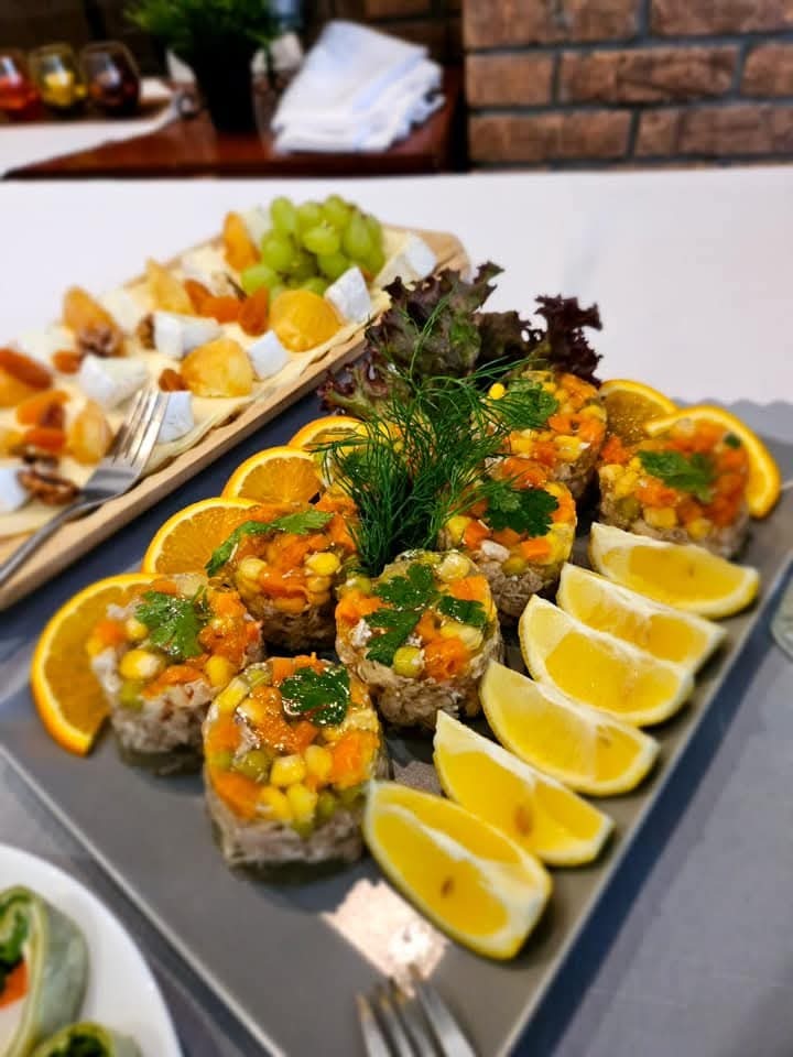 Elegancko podane przystawki: galaretki z warzywami i ziołami, plastry pomarańczy i cytryny na szarym talerzu, w tle deska serów z owocami.