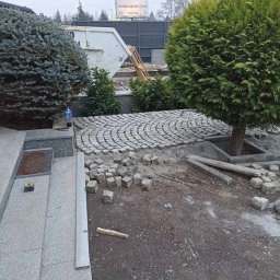 BVM Brykarstvo - Fragment ogrodu w trakcie prac: ułożona część okrągłej ścieżki z kostki granitowej, obok leżą nieułożone kostki, widoczne narzędzia i roślinność. Prace brukarskie w toku.