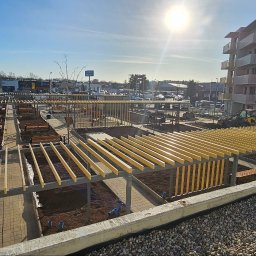 BVM Brykarstvo - Nowoczesny park osiedlowy z pergolami i ścieżkami z kostki. W tle budynki mieszkalne i plac budowy z koparką. Słoneczny dzień, widok z góry.