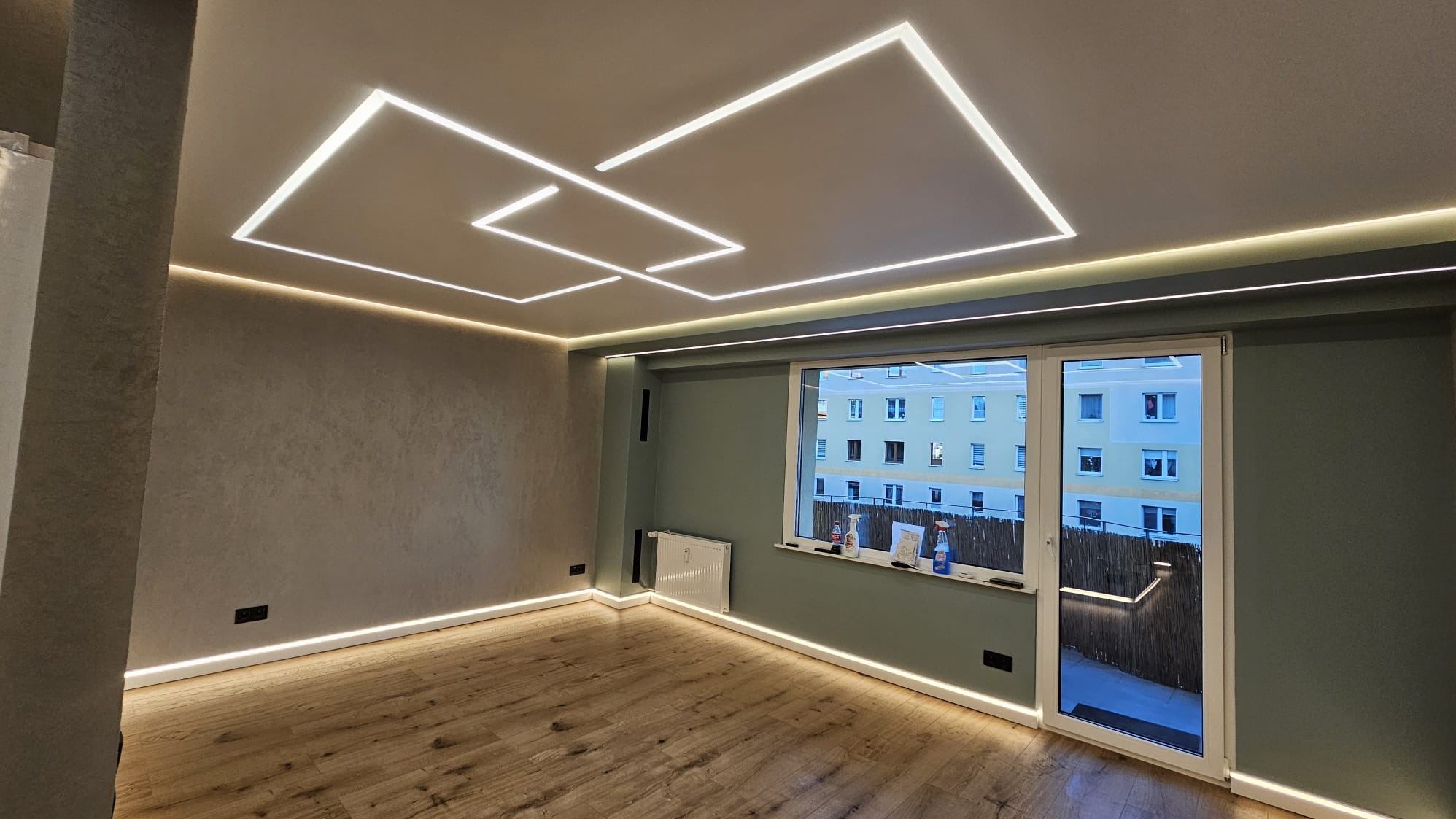 Nowoczesne oświetlenie LED w salonie: geometryczne wzory na suficie, listwy przypodłogowe, parkiet. Widok na balkon przez okno.