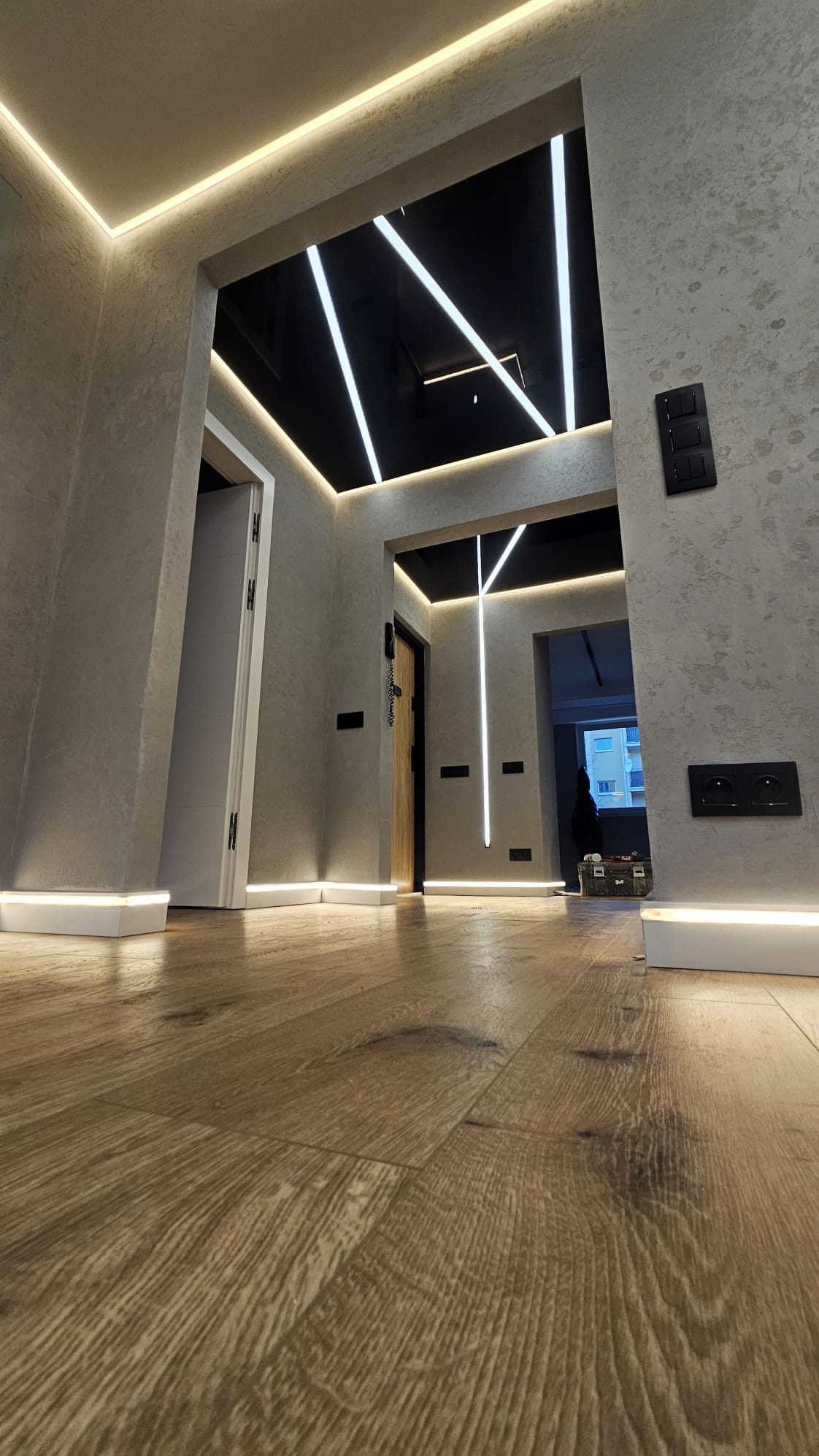 Nowoczesny korytarz z oświetleniem LED w suficie i podłodze, ściany w odcieniach szarości, drewniana podłoga. Ujęcie z niskiej perspektywy.