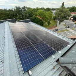 OZE-ELECTRA - Panele fotowoltaiczne na metalowym dachu budynku, widok z góry, z fragmentem ulicy i zieleni w tle. Instalacja fotowoltaiczna.