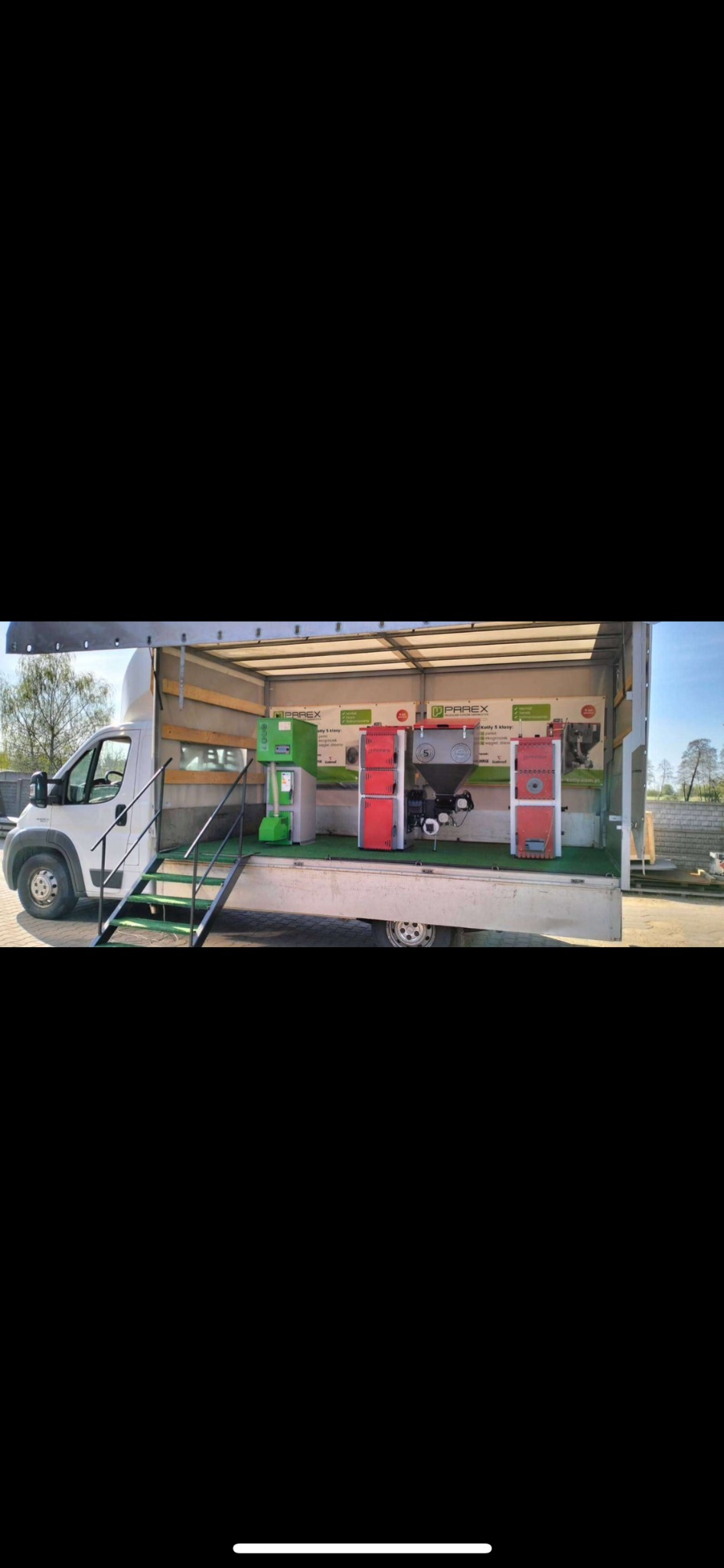 Mobilna ekspozycja kotłów Parex wewnątrz białego busa z schodami. Prezentacja modeli kotłów na paliwo stałe w przestrzeni wystawienniczej.