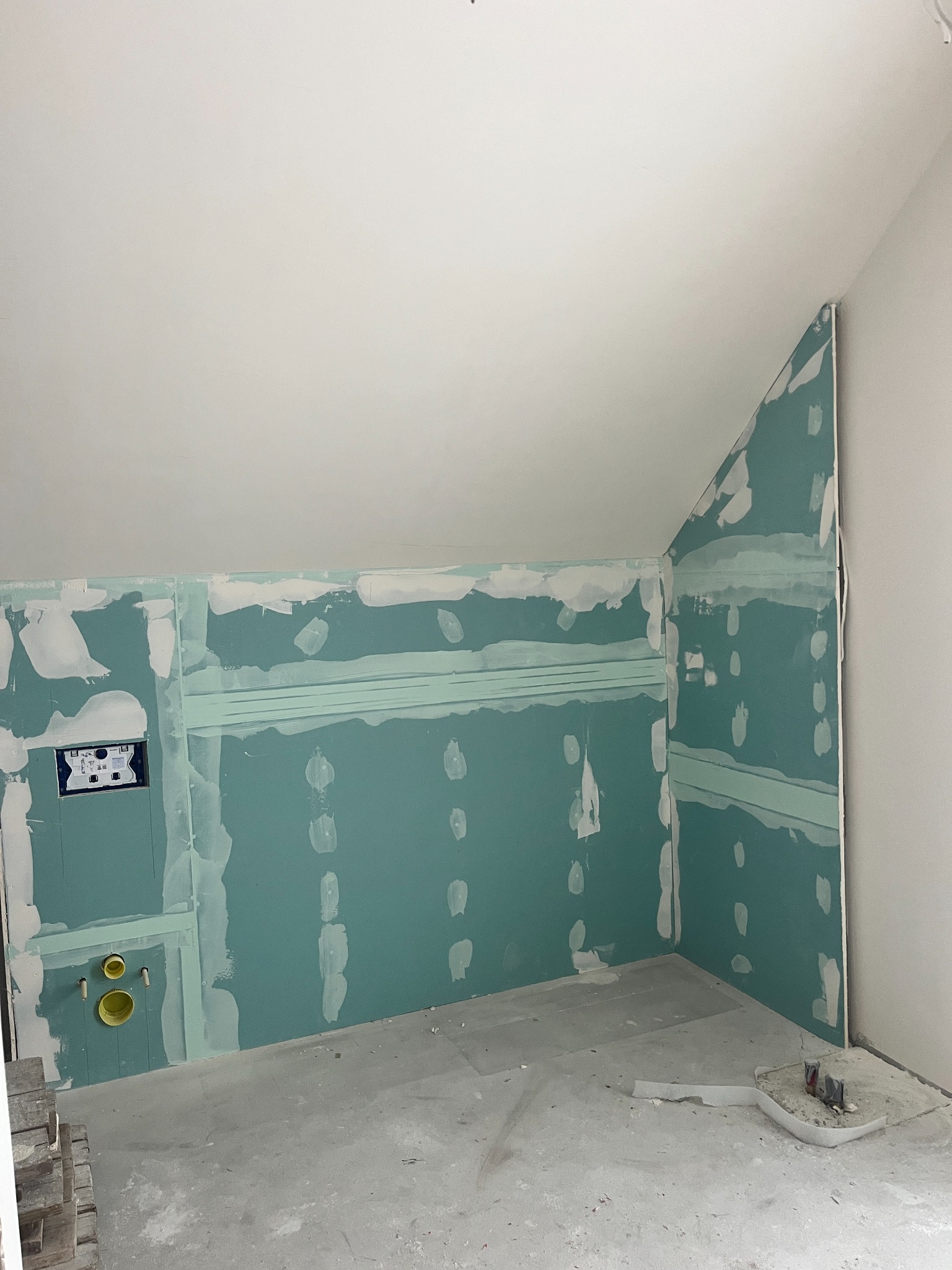 Poddasze w trakcie adaptacji na łazienkę. Widoczne płyty gipsowo-kartonowe na ścianach ze śladami szpachlowania i instalacją podtynkową. Skos dachu.