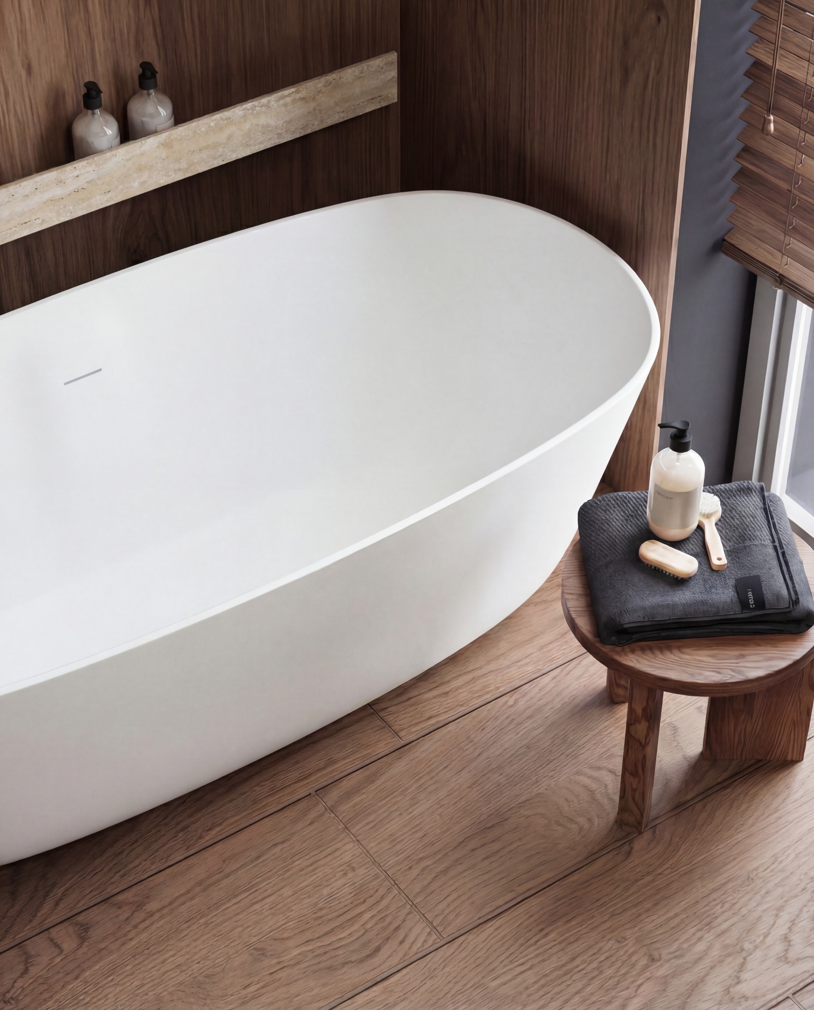 Nowoczesna, owalna wanna wolnostojąca w minimalistycznej łazience z drewnianymi akcentami i podłogą. Na stołku ręcznik, mydło i szczotki do ciała.