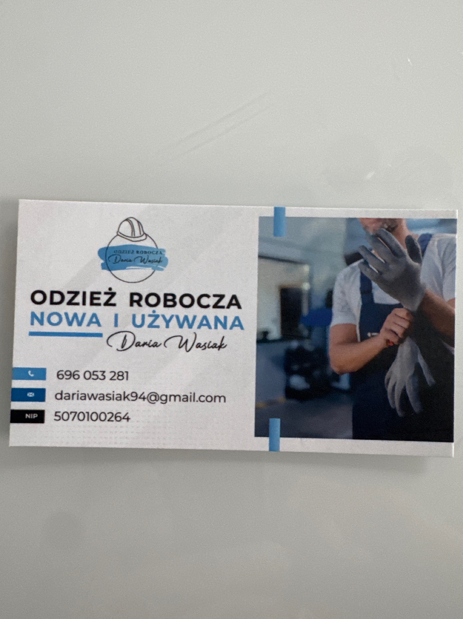 Wizytówka firmy oferującej nową i używaną odzież roboczą z ilustracją pracownika w kombinezonie i rękawicach, oraz danymi kontaktowymi.