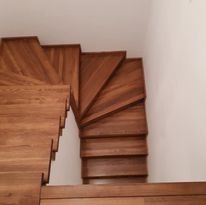 Kątowe ujęcie na ciemne, drewniane schody z wyraźnym usłojeniem, prowadzące w dół wzdłuż białej ściany. Widoczne detale wykończenia i naturalna kolorystyka drewna.