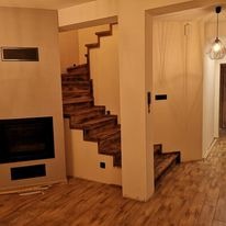 Klatka schodowa z drewnianymi schodami w nowoczesnym wnętrzu. Widoczne oświetlenie i wykończenie kominka. Ujęcie z dołu, podkreślające detale.