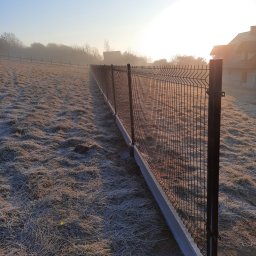 P&P - Nowoczesne ogrodzenie panelowe z podmurówką betonową, widok z perspektywy pola pokrytego szronem, w tle dom i drzewa w porannej mgle.