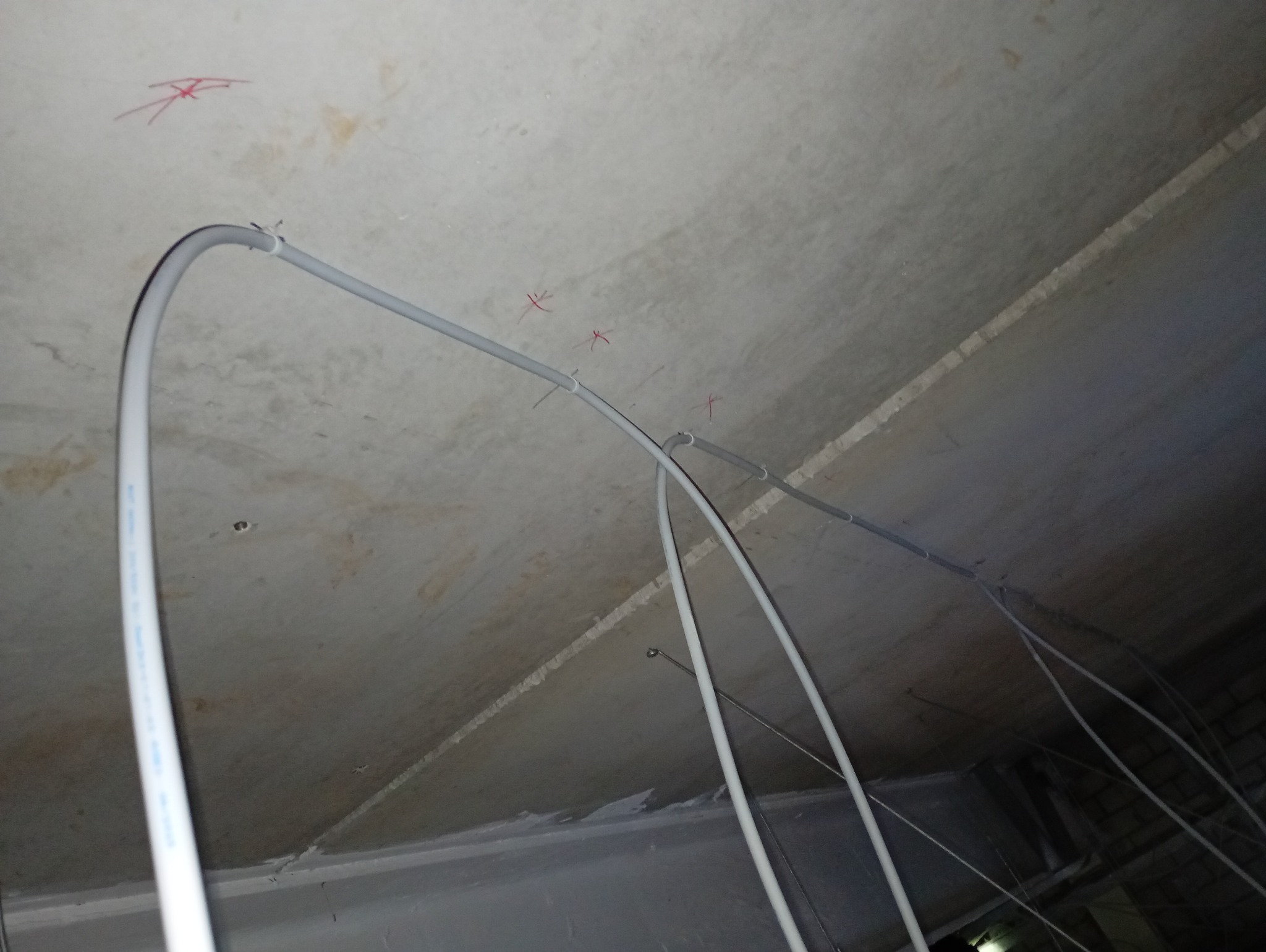 Szare rurki instalacyjne przymocowane do sufitu z betonu, widoczne czerwone oznaczenia. Ujęcie z dołu, perspektywa ukośna, sufit z widocznymi łączeniami płyt.