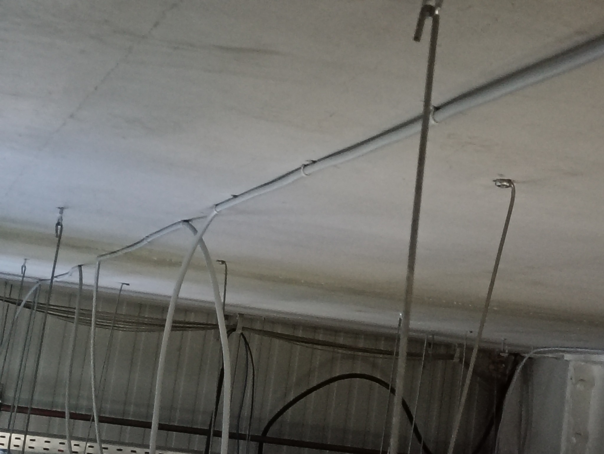 Szare rury i metalowe uchwyty pod sufitem, widok z dołu. Elementy instalacji w surowym wnętrzu, prawdopodobnie w trakcie montażu.