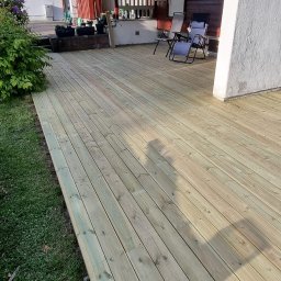 Wiercimy Temat - Nowa, jasna deska tarasowa z widocznymi śladami montażu, przylegająca do domu z markizą. Dwa krzesła ogrodowe w tle, cień osoby na deskach.