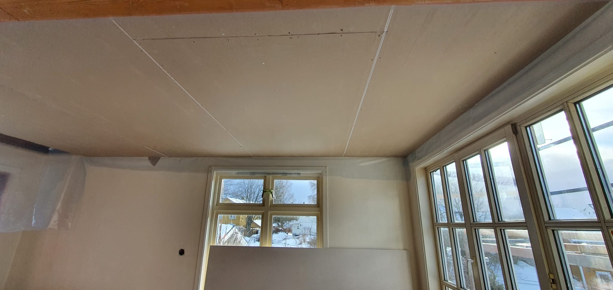 Zamontowany sufit z płyt gipsowych w jasnym pomieszczeniu z oknami. Widoczne łączenia płyt i przygotowanie do dalszych prac wykończeniowych.