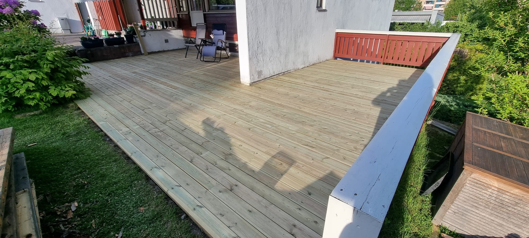 Nowa, jasna deska tarasowa z widocznymi cieniami, otoczona zielenią i elementami architektury. Świeżo położona deska tarasowa.