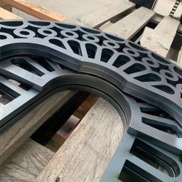 Metal Idustry Company Sp z O.O. - Metalowe elementy z wyciętymi wzorami, ułożone na drewnianej palecie. Precyzyjne cięcie, powtarzalny wzór, surowy materiał. Detal obróbki metalu.