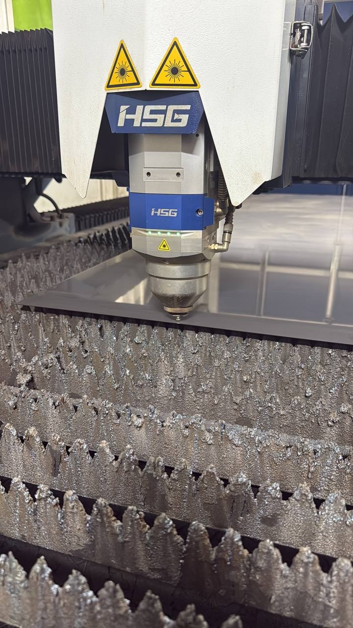 Laserowe cięcie metalu na maszynie CNC HSG. Precyzyjna obróbka blachy, widoczne iskry i detale urządzenia. Nowoczesna technologia w procesie produkcyjnym.