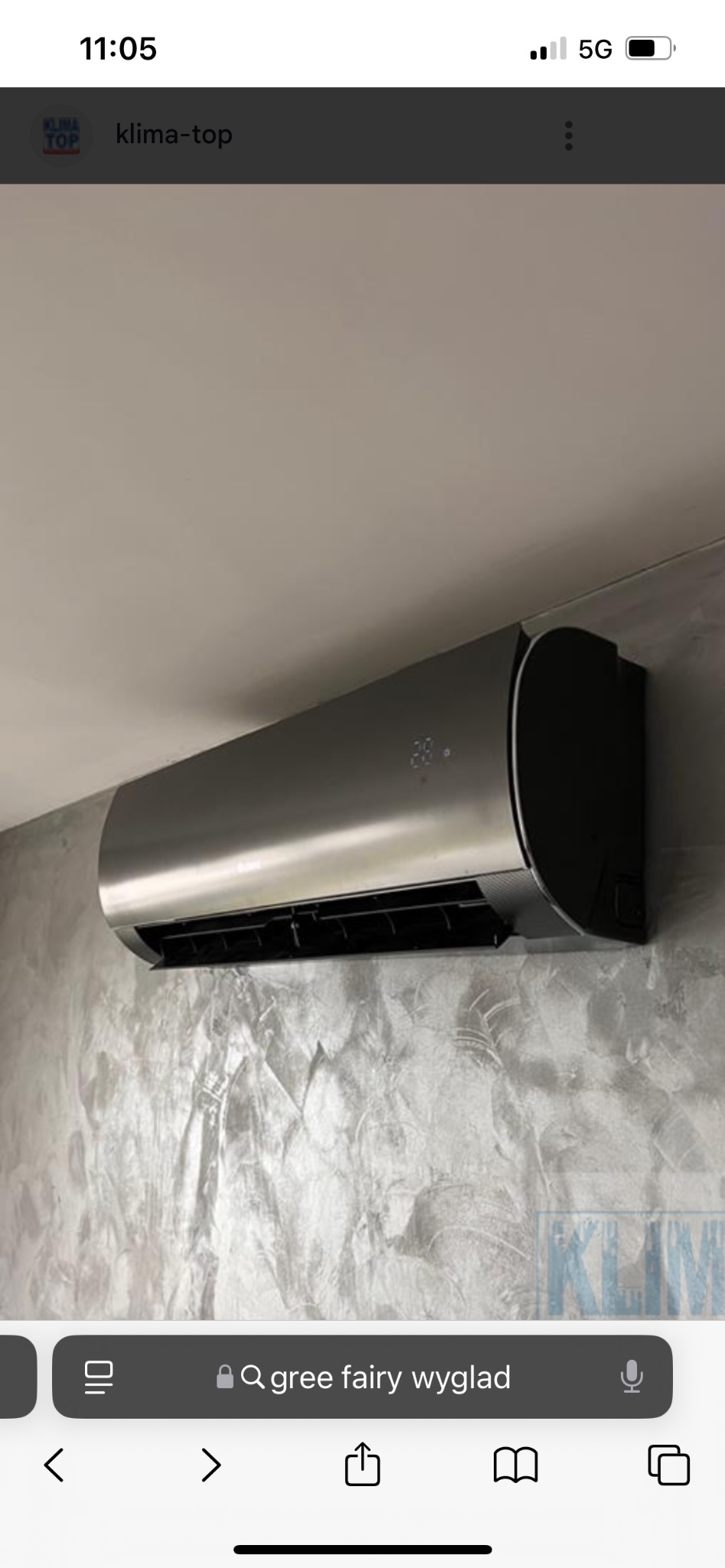 Nowoczesny klimatyzator ścienny w kolorze srebrnym, zamontowany na ścianie o fakturze betonu. Widoczny wyświetlacz temperatury. Minimalistyczny design.