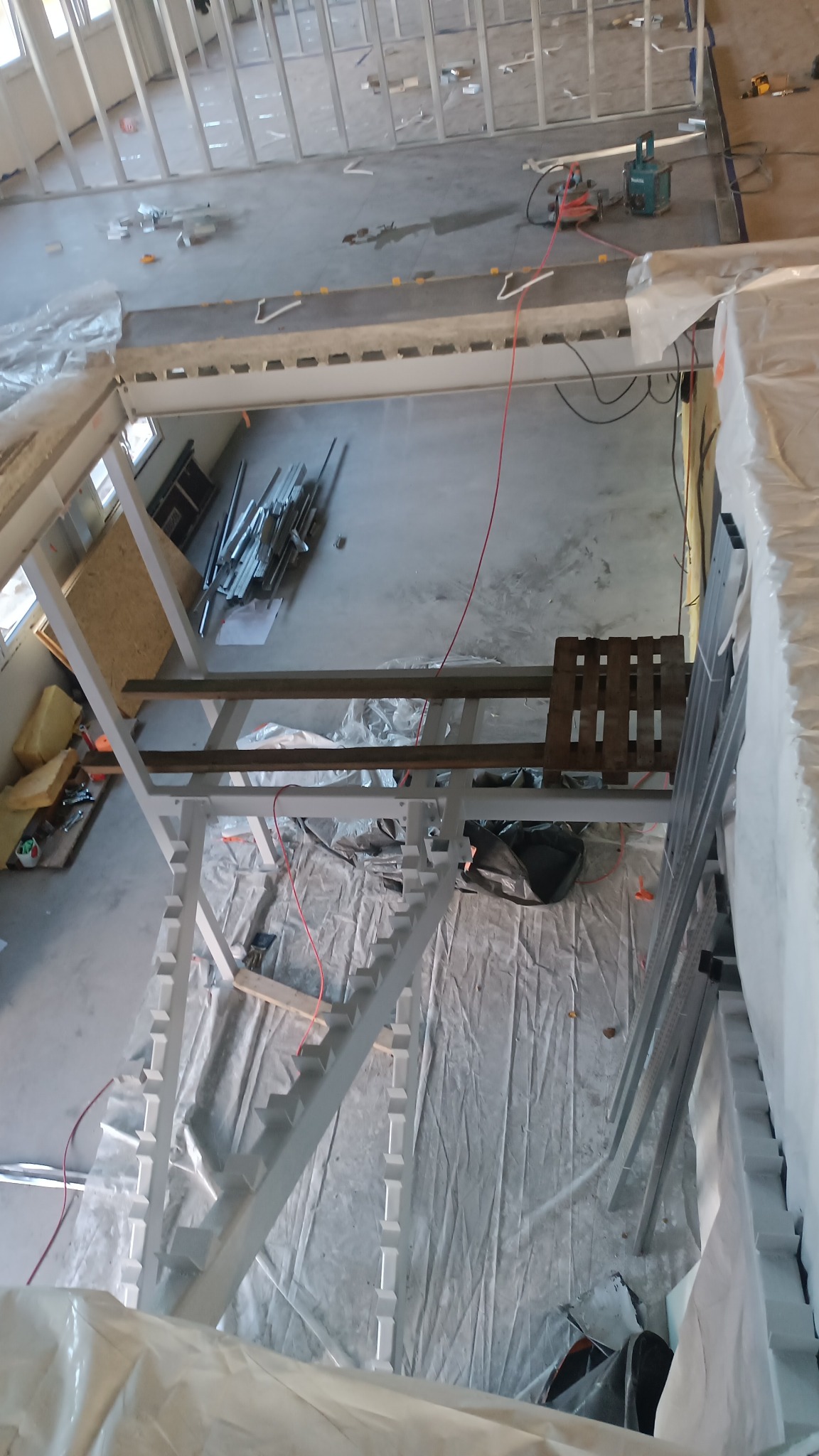 Wnętrze w budowie: metalowa konstrukcja schodów dwubiegowych przygotowana pod wylanie stopni betonowych. Widok z góry na surowy stan prac.