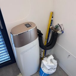 TUBERO - Zmiękczacz wody Golden z podłączeniem hydraulicznym, obok torba z tabletkami solnymi Aqua Pro. W tle poziomica. Widok na instalację w rogu pomieszczenia.