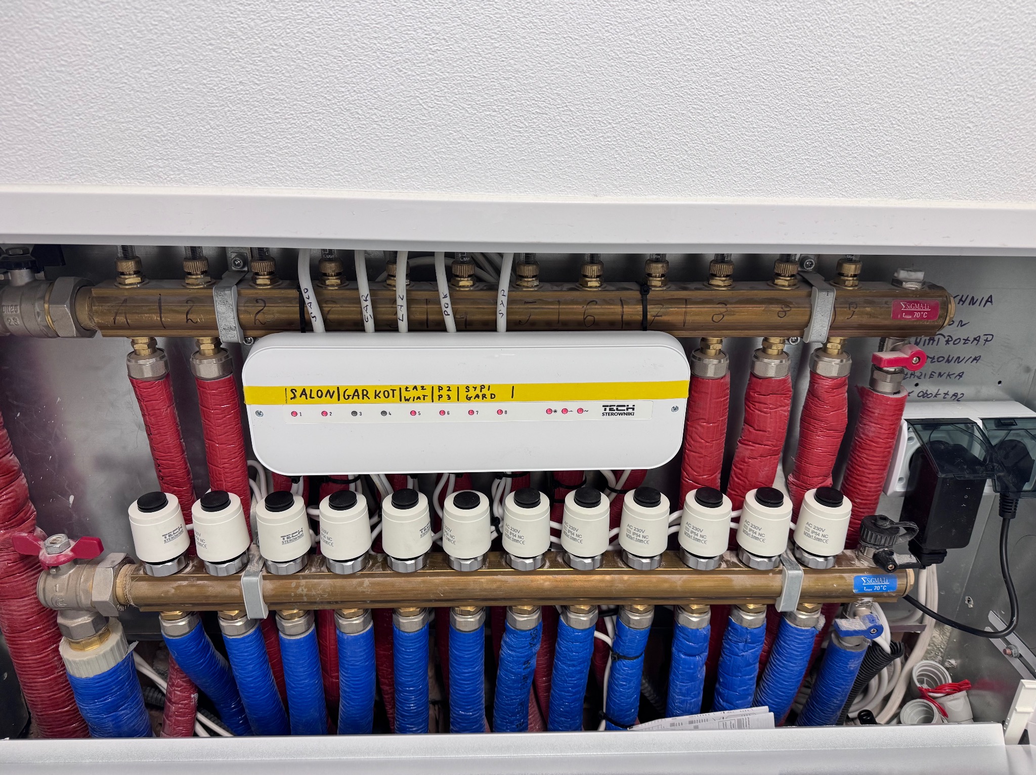 Rozdzielacz ogrzewania podłogowego z automatyką TECH Sterowniki, rury w izolacji czerwonej i niebieskiej. Instalacja wykonana w Przyborowie.