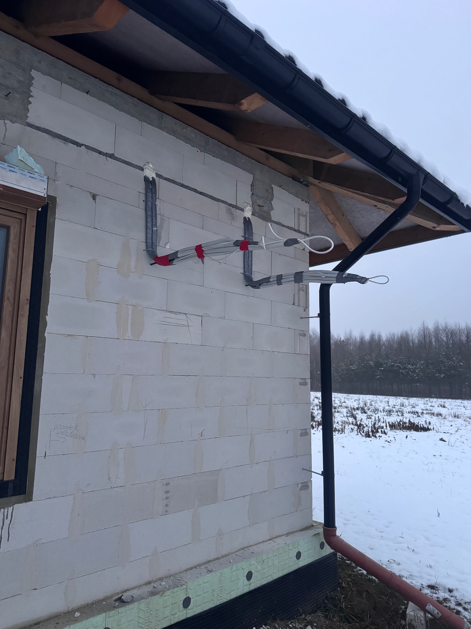 Montaż instalacji na zewnątrz budynku w zimowej scenerii. Rury przymocowane do ściany z betonu komórkowego, widoczne elementy izolacji i orynnowanie.