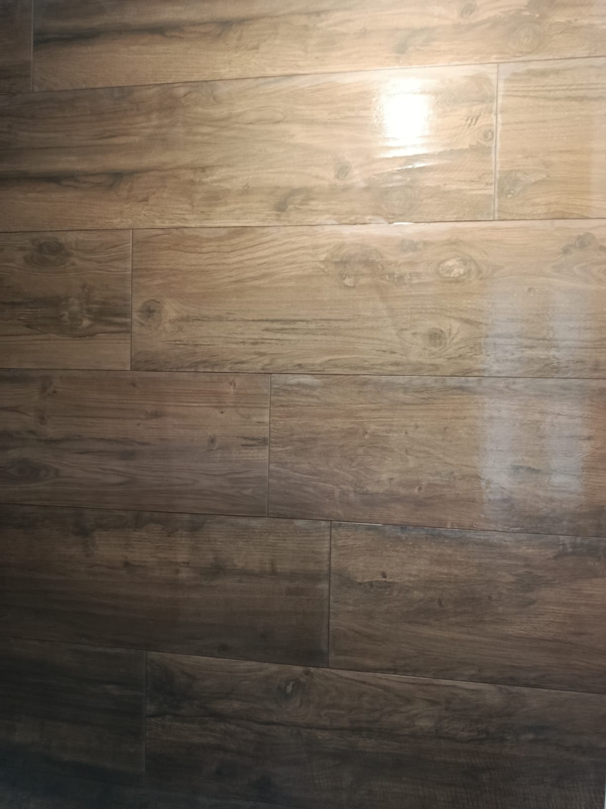 Ułożone, brązowe płytki podłogowe imitujące drewno, z widoczną strukturą słojów i połyskiem, tworzące ciepły i naturalny wygląd podłogi.