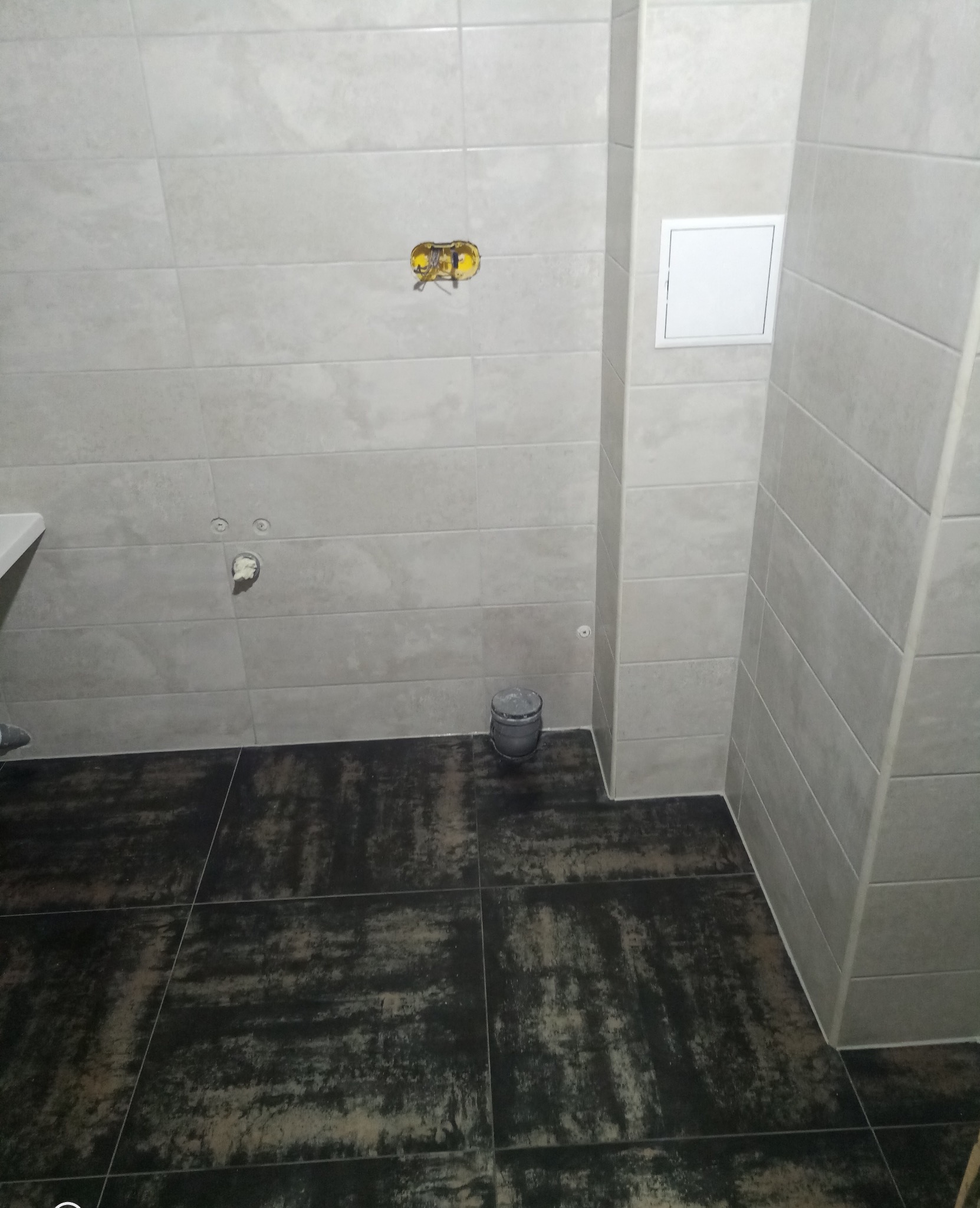 Wykończona łazienka w Bolesławcu z beżowymi płytkami ściennymi i ciemną podłogą. Widoczne przyłącza hydrauliczne i elektryczne, gotowe do montażu armatury.