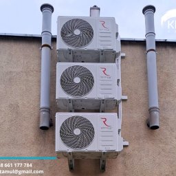 KlimArt-Serwis Klimatyzacja - Trzy klimatyzatory Rotenso zamontowane jeden nad drugim na elewacji budynku, z widocznymi rurami odprowadzającymi. Ujęcie z dołu, podkreślające pionowy układ.
