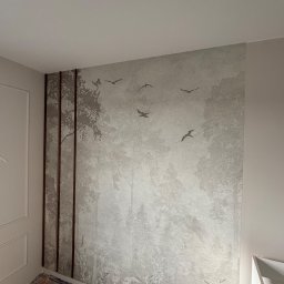 M.W.INVEST - Ściana z tapetą w leśny motyw z sylwetkami ptaków, ozdobiona pionowymi listwami. Podłoga przygotowana do dalszych prac wykończeniowych.