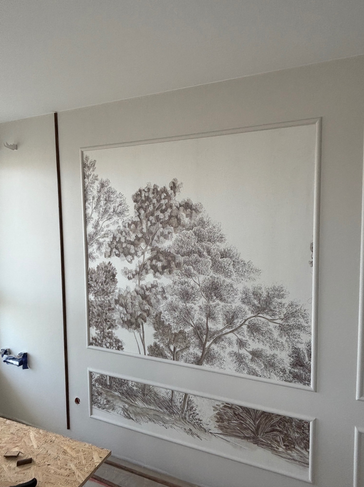 Dekoracyjna ściana z ręcznie malowanym motywem leśnym w ramie, z widocznymi detalami wykończenia i subtelnym oświetleniem, tworząca unikalny element wystroju wnętrza.