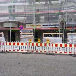 Thermo-plast Sp.z o.o. - Budynek w rusztowaniach, zabezpieczony barierami z żółtymi lampami ostrzegawczymi. Widoczne okna i drzwi w folii ochronnej. Prace remontowe w toku.