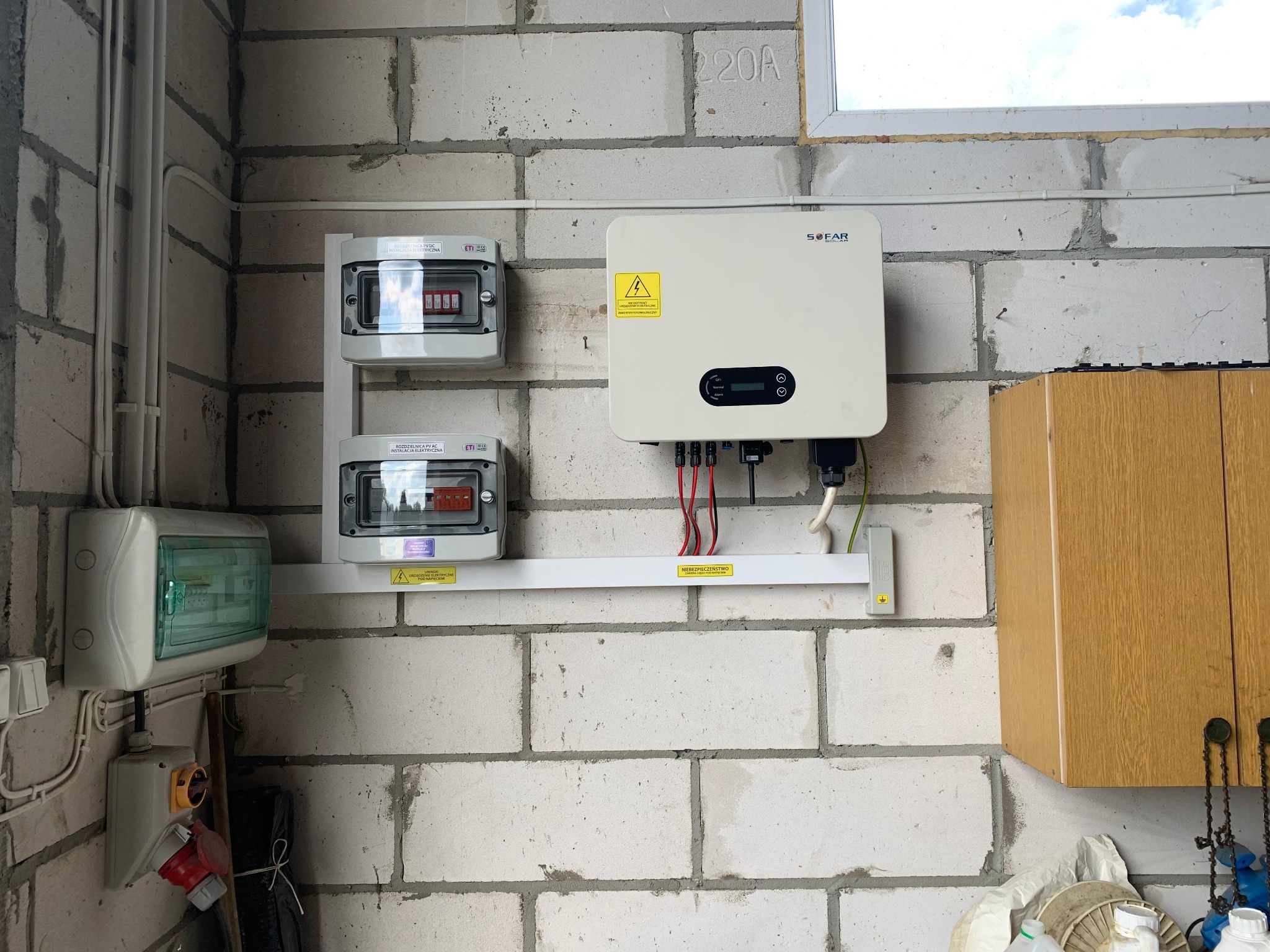 Instalacja fotowoltaiczna wewnątrz budynku: inwerter Sofar Solar, rozdzielnice elektryczne na ścianie z białego bloczka, widoczne okablowanie i elementy zabezpieczeń.