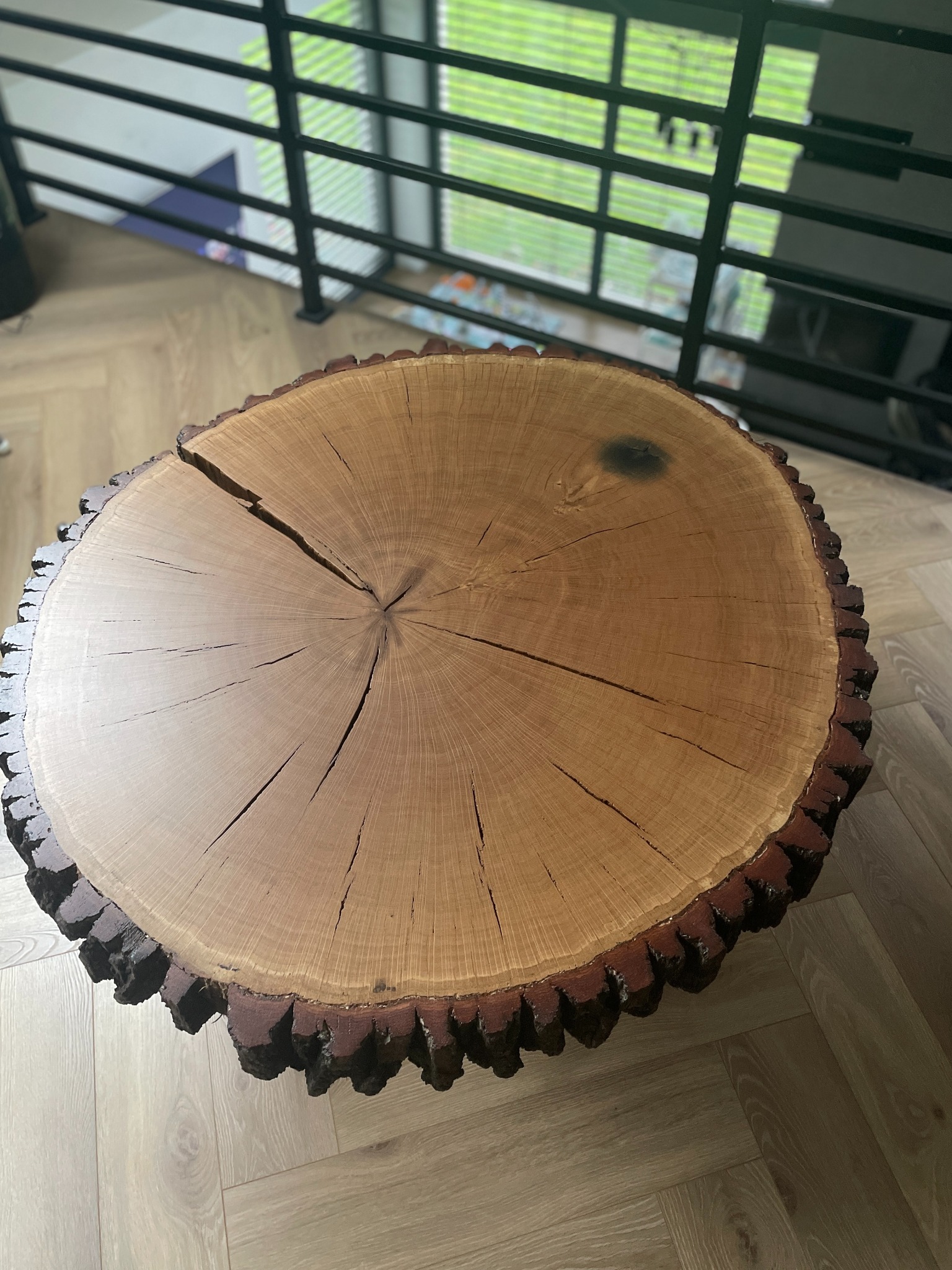 Okrągły stolik kawowy z litego drewna dębowego z wyraźnym rysunkiem słojów i naturalną krawędzią, na tle parkietu i balustrady.