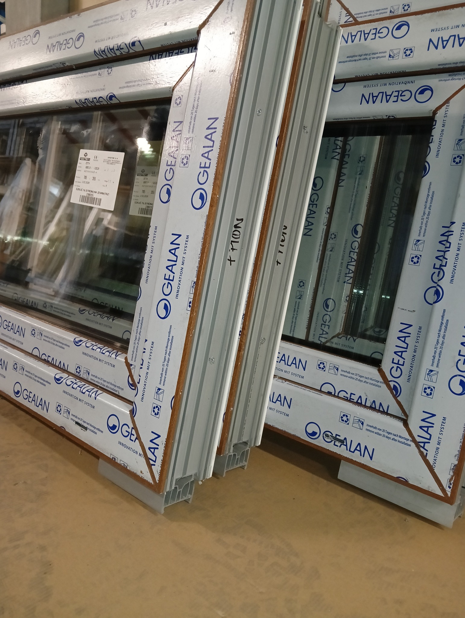 Nowe okna PCV marki Gealan, zabezpieczone folią ochronną z nadrukiem, czekają na montaż. Widoczne etykiety i napisy informacyjne na profilach.
