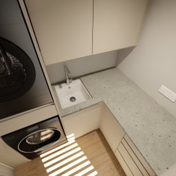 Chicc Interiors - Projekt małej, funkcjonalnej łazienki z pralką, suszarką, umywalką w blacie z szarego lastryko i podgrzewaczem wody. Nowoczesny design, jasne kolory, minimalistyczne wykończenie.