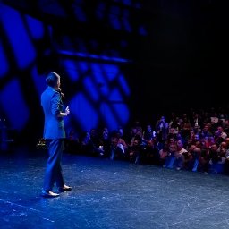 Ilona Sodolska - Ekspert od kolorów w biznesie - Prelegentka w niebieskim garniturze przemawia do publiczności na scenie oświetlonej niebieskim światłem. Tłum słuchaczy siedzi na widowni.