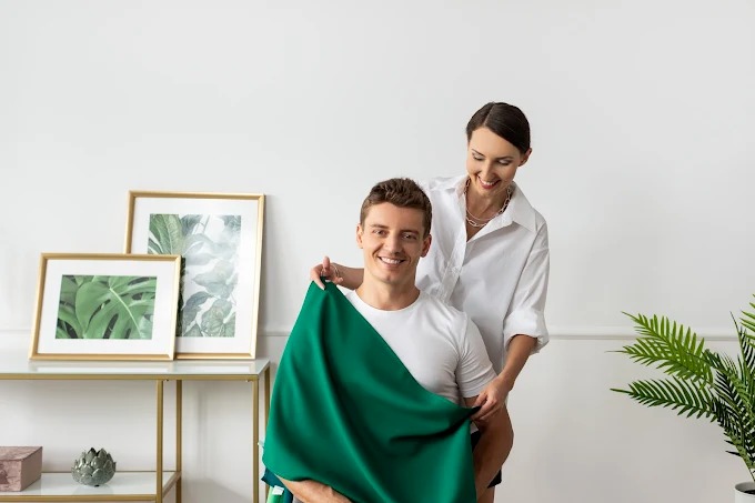 Konsultacja kolorystyczna: uśmiechnięty mężczyzna z zielonym materiałem, doradca w białej koszuli dobiera odcień. W tle minimalistyczny wystrój wnętrza.