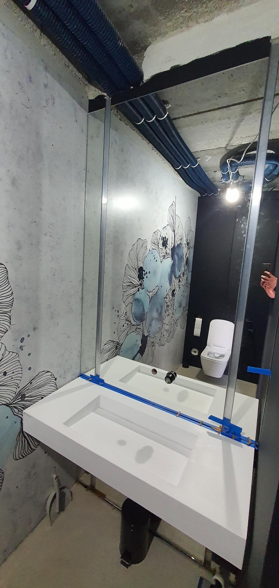 Nowoczesna łazienka w Łodzi z umywalką wpuszczaną w blat, lustrem w metalowej ramie i dekoracyjną tapetą. Widoczne rury pod sufitem.