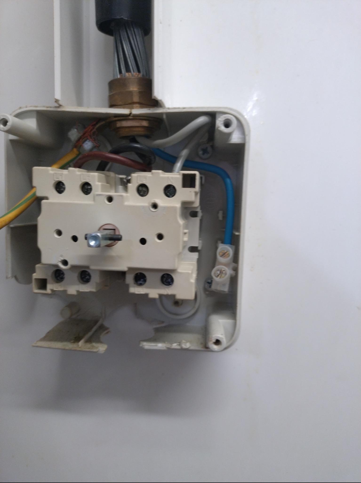 Otwarta, uszkodzona puszka elektryczna z widocznymi przewodami i elementami złącznymi. Widoczne ślady uszkodzeń na obudowie.