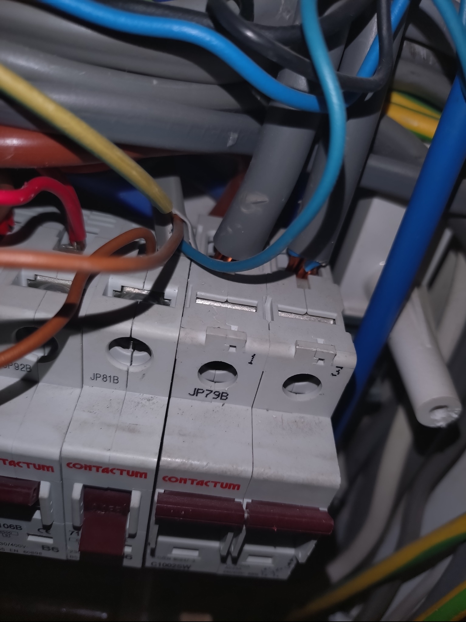 Szczegółowe ujęcie instalacji elektrycznej z widocznymi bezpiecznikami Contactum i różnokolorowymi przewodami. Widoczne oznaczenia JP81B i JP79B na obudowach.
