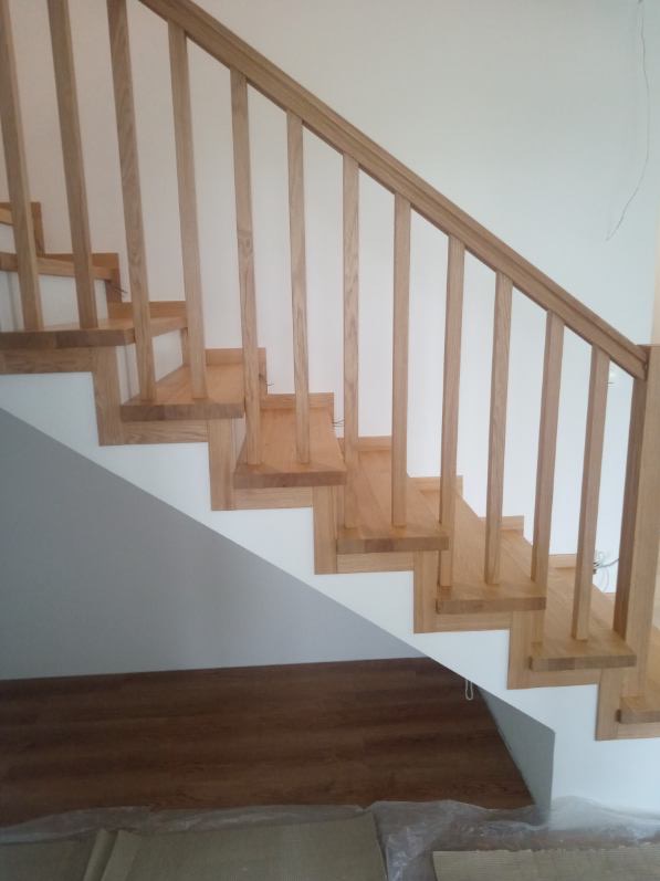 Jasne, drewniane schody z balustradą w nowoczesnym wnętrzu. Widoczne detale konstrukcyjne i naturalne wykończenie drewna. Ujęcie z dołu, podkreślające geometrię.