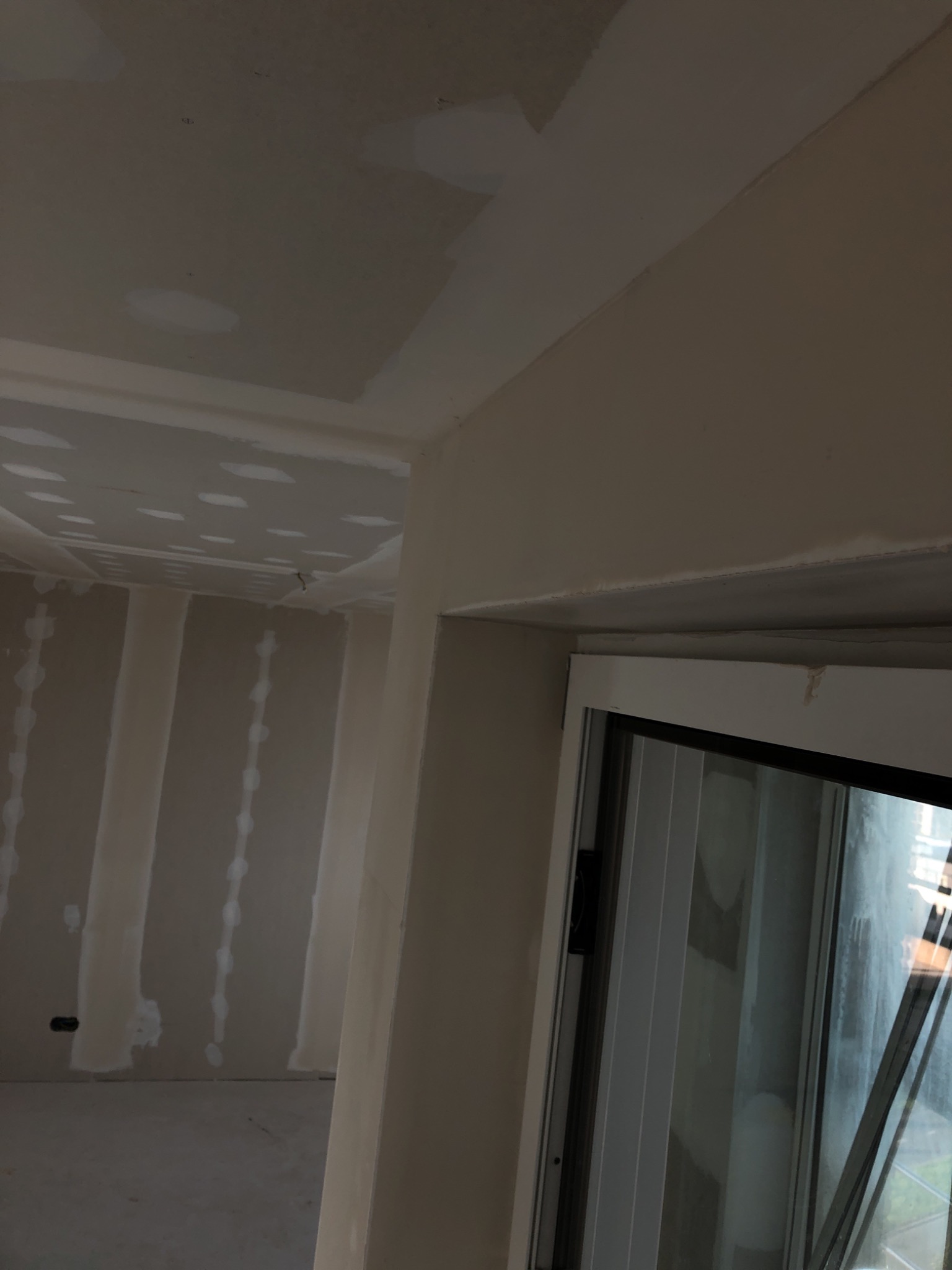 Wnętrze w trakcie prac wykończeniowych: ściany z płyt gipsowo-kartonowych, widoczne łączenia, przygotowane do dalszych etapów prac. Fragment okna w prawym dolnym rogu.