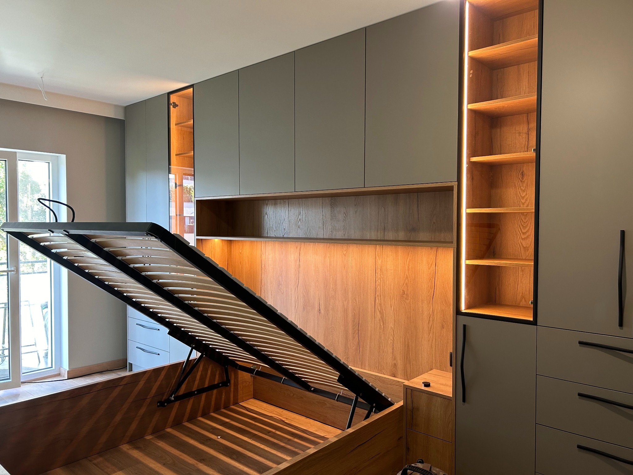 Nowoczesna szafa wnękowa z łóżkiem z podnoszonym stelażem, drewniane wykończenie, szare fronty, oświetlenie LED. Funkcjonalne rozwiązanie do sypialni.